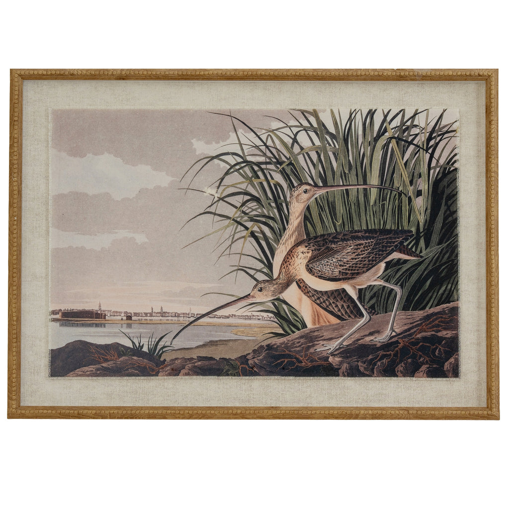 Front view of a framed print showing two long-billed wading birds beside reeds and water, bordered by a pale textured surround and tan-gold beaded frame.