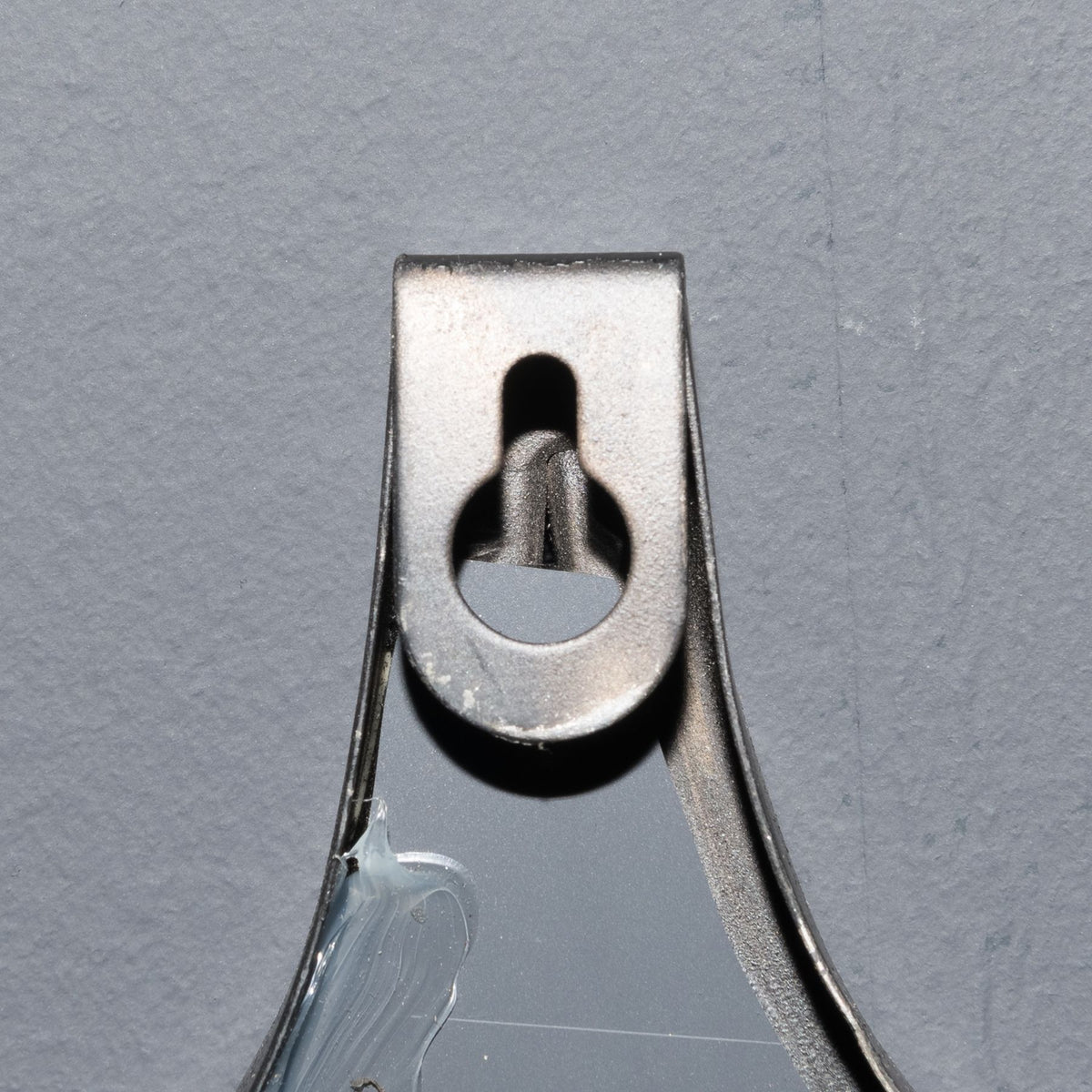 Close-up of the mirror's reverse showing a keyhole-shaped opening in a small plate against the grey backing.
