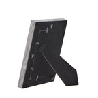 Rear view of the photo frame with its black folding easel extended, retaining tabs around the backing and hanging loops visible.