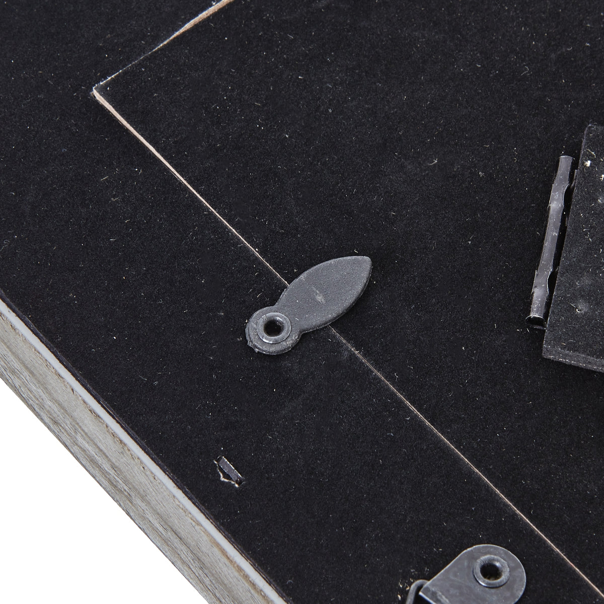 Close-up of a rotating retaining tab across the edge of the black rear panel, with the easel hinge visible to the right.