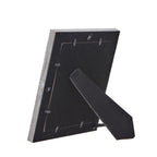 Rear view of the photo frame with its black folding easel extended, retaining tabs around the backing and two hanging loops.