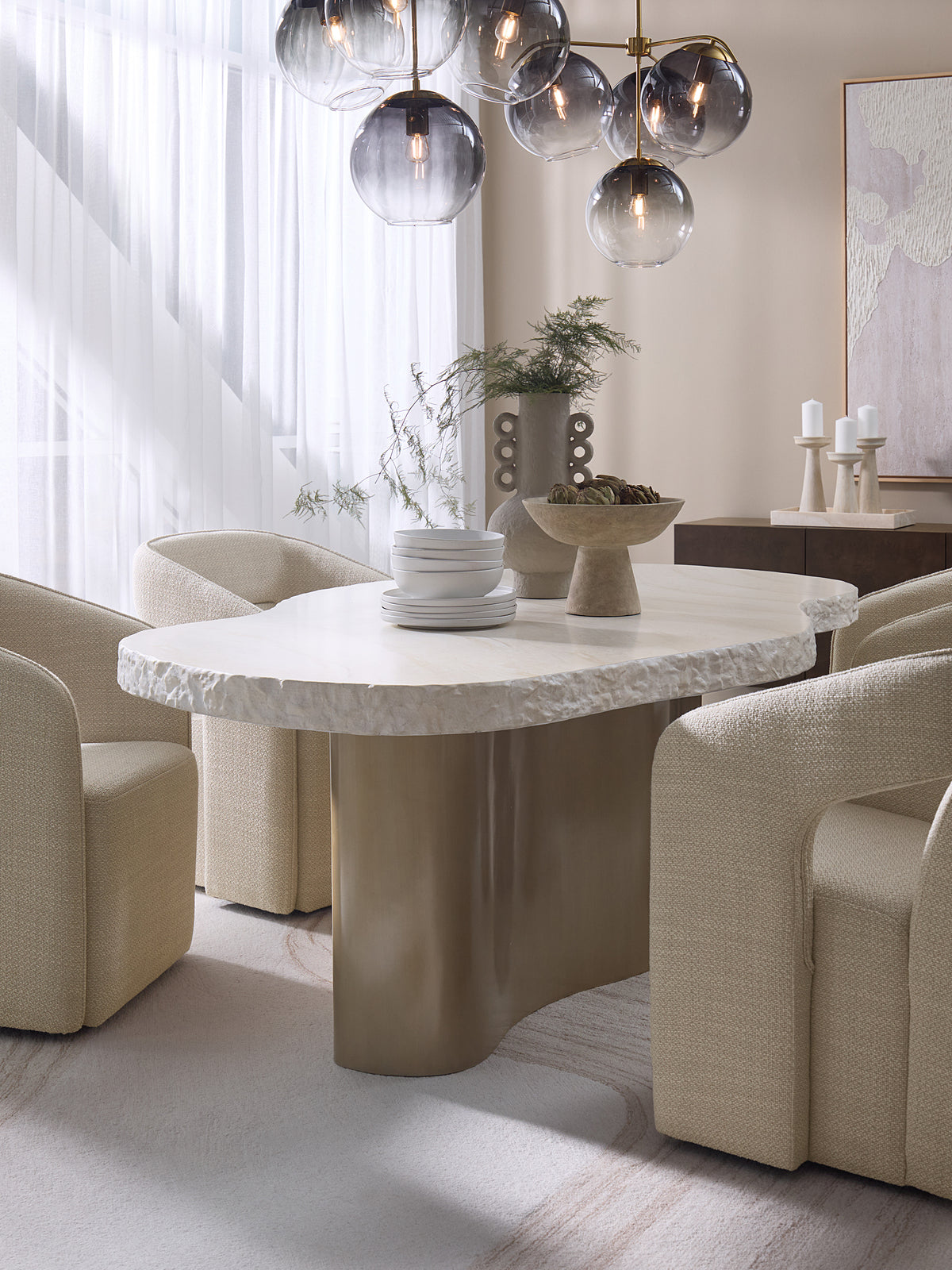 Waveline dining table with cream upholstered chairs, stacked crockery and sculptural vessels beneath a glass globe pendant.