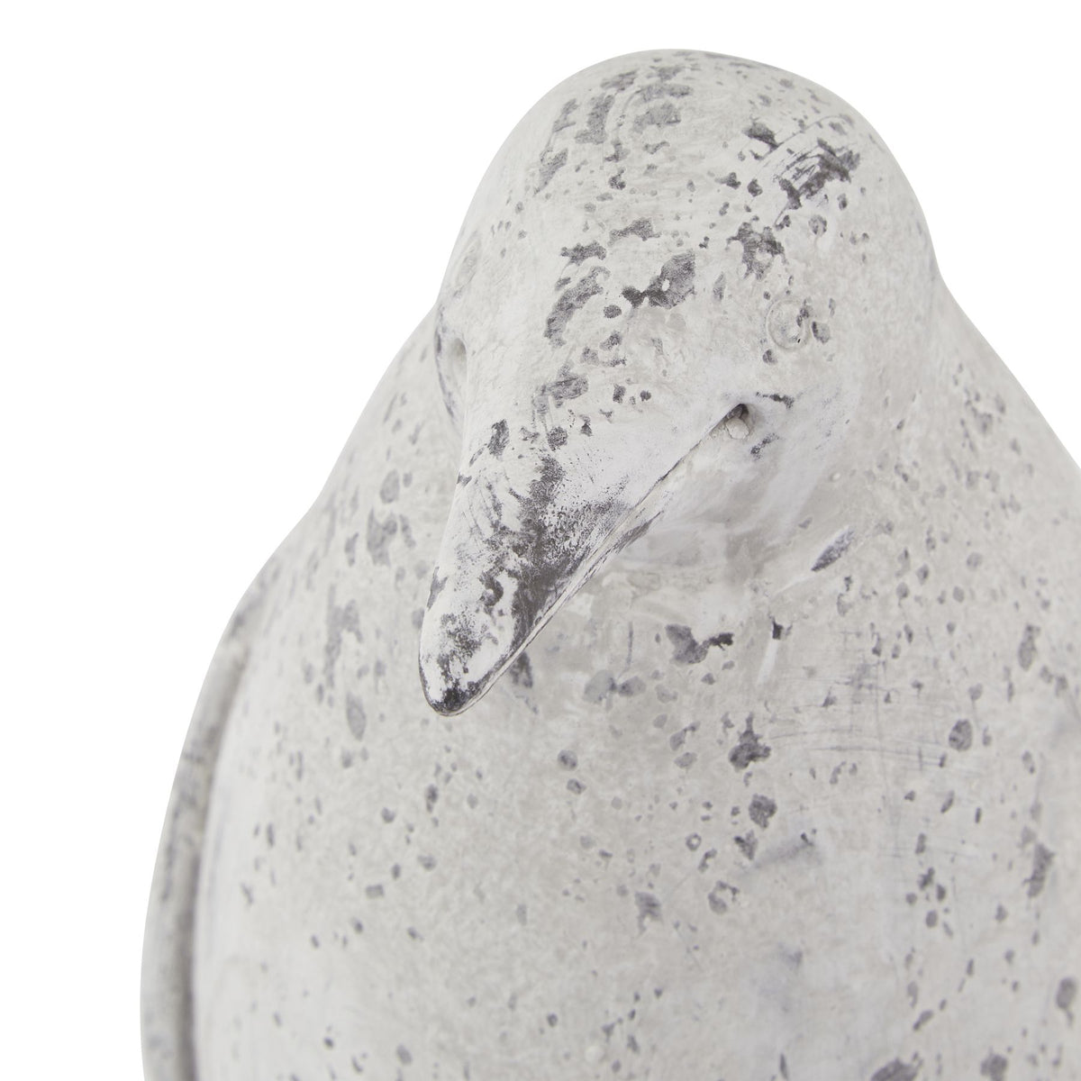 Close-up of the penguin ornament's head and short beak, with a small round eye and scattered grey markings across the pale surface.