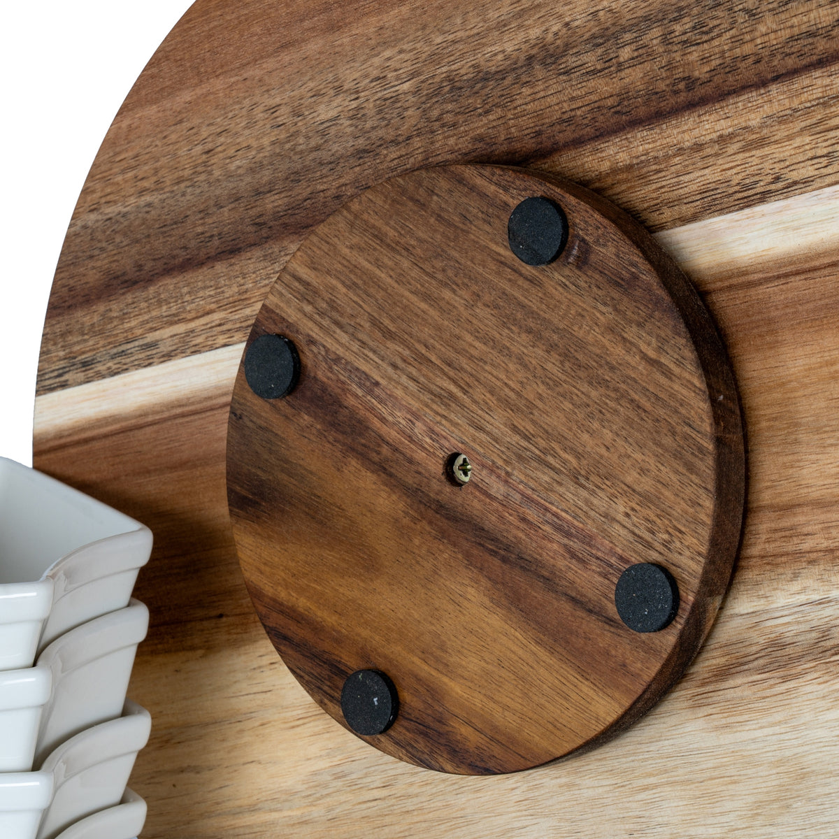 Close-up of the circular underside base plate showing a central fastener and four black pads, beside part of the stacked white dishes.