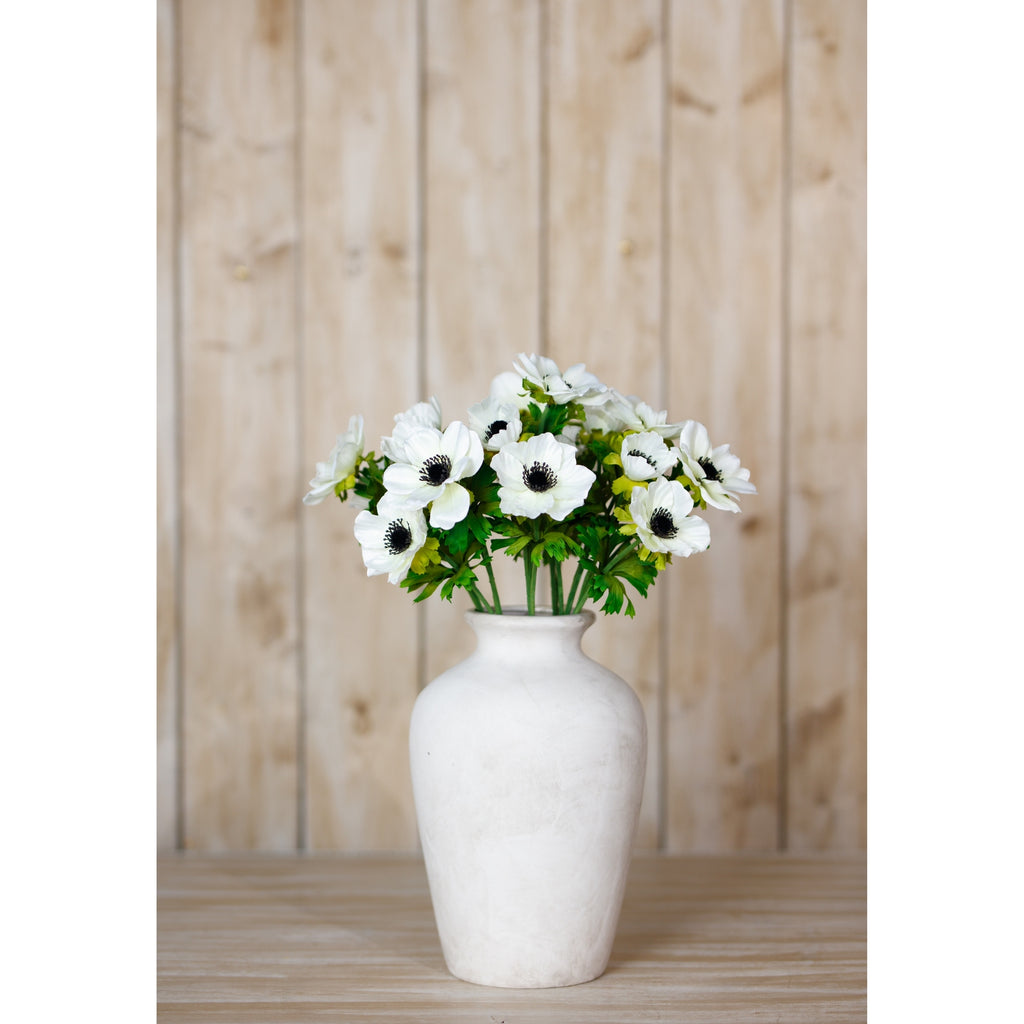 White anemone flowers arranged in a rounded white vase on a pale wooden surface against vertical wood panelling.