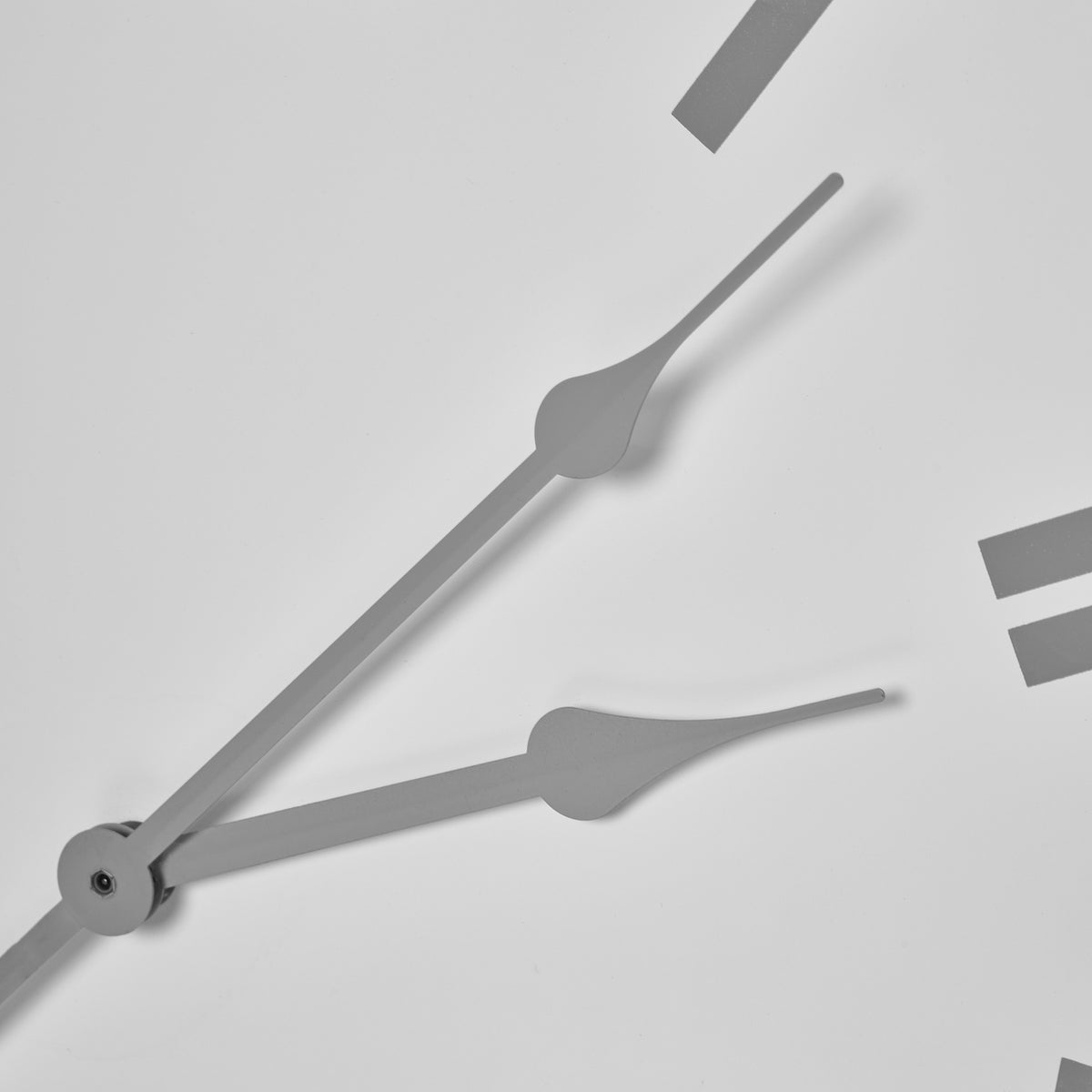 Close-up of the shaped grey clock hands and central fixing against the plain white face, with portions of Roman numerals visible.