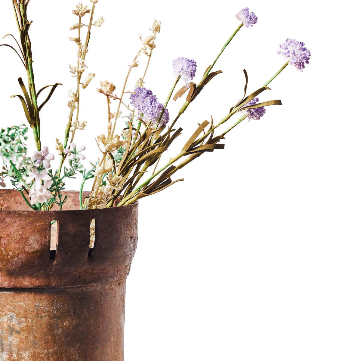 Close view of lilac flowerheads, cream sprigs and green foliage spreading from a weathered brown vessel with slots near the rim.