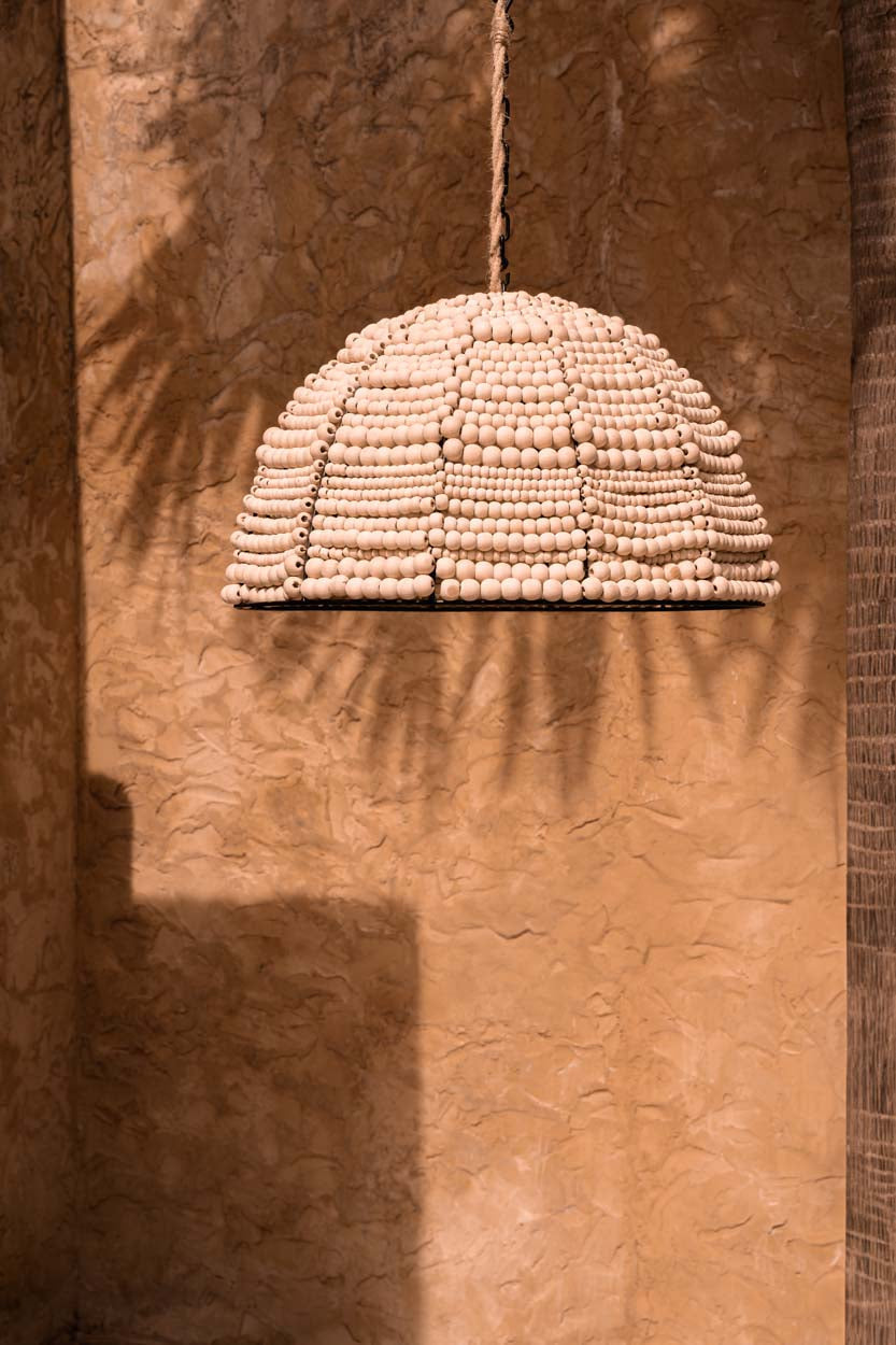 Wooden Bead Dome Pendant Light – Natural — styled against a warm wall