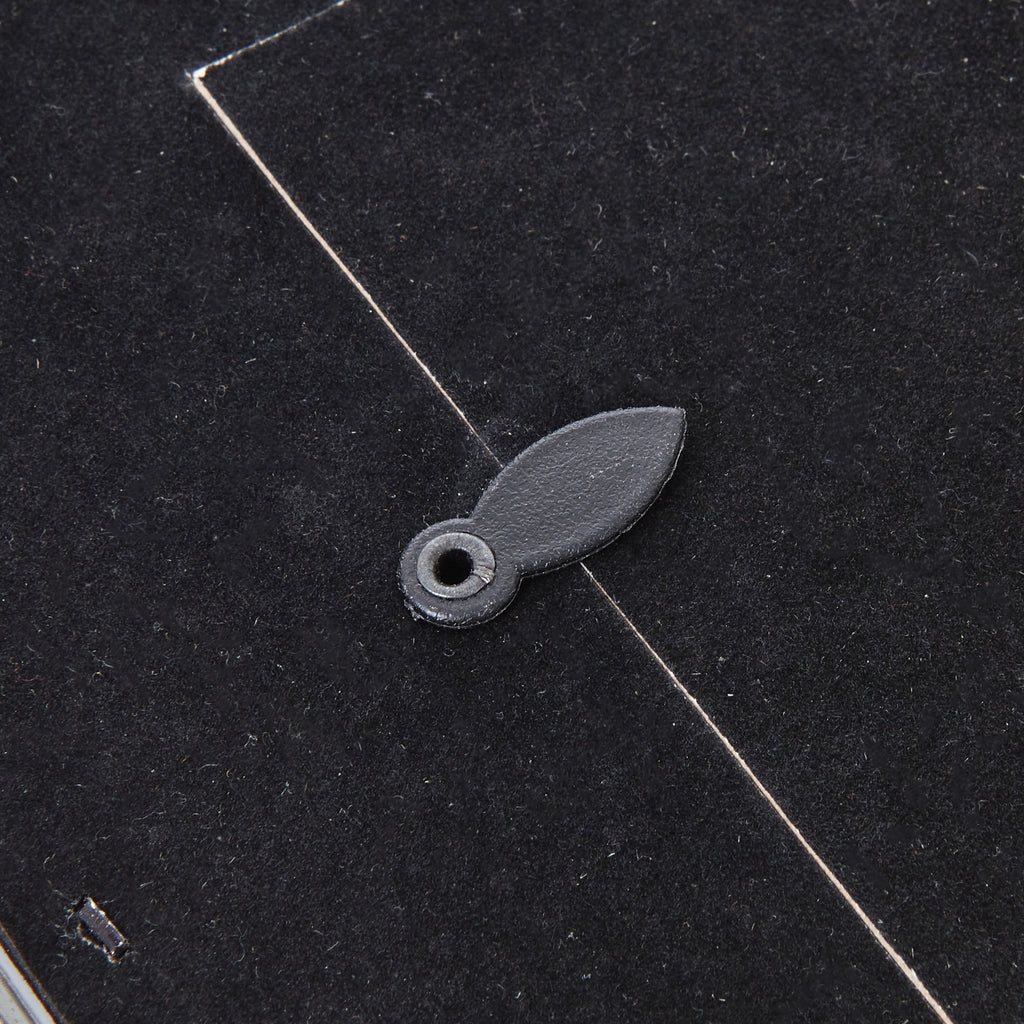 Detail of an oval turn tab overlapping the edge of the photo frame's dark rear panel.