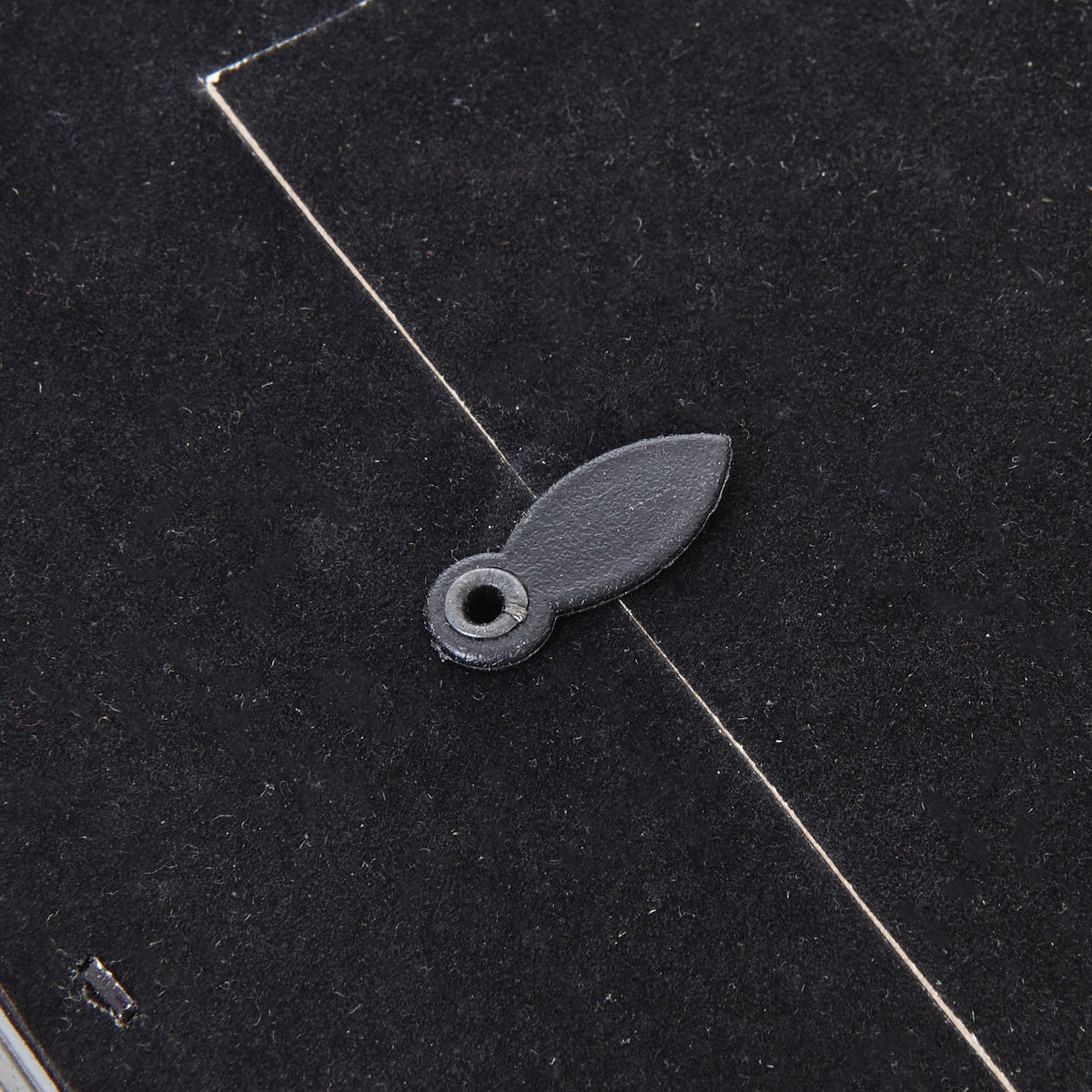 Detail of an oval turn tab overlapping the edge of the photo frame's dark rear panel.