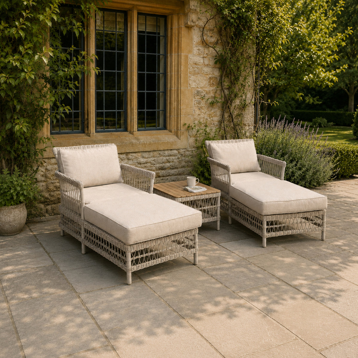 Woven loungers with pale seat and back cushions beside a stone wall and climbing greenery, with a mug and reading material on the table between them.