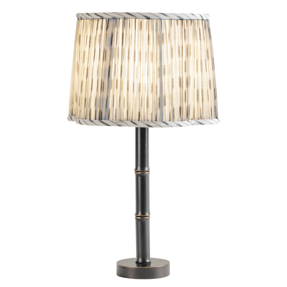 Illuminated table lamp showing light through the gathered fabric shade, with dark ikat markings still visible.