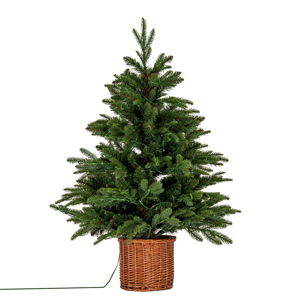 Green artificial Christmas tree with an uneven tapered outline in a brown woven pot cover, with a green cable trailing to the left.
