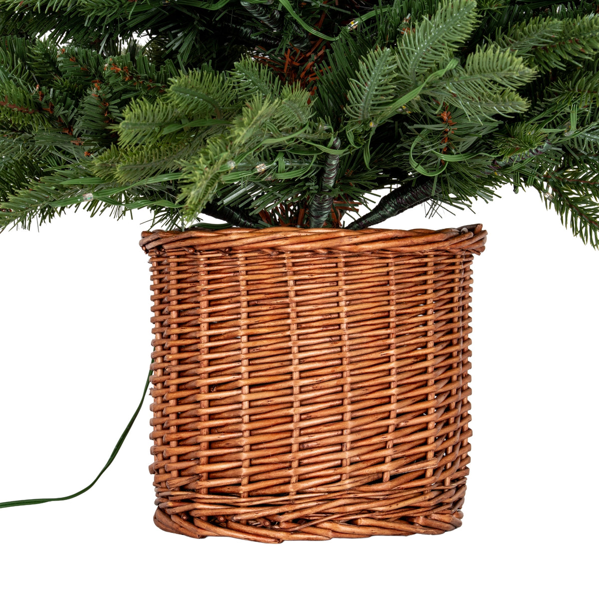 Brown woven pot cover beneath the tree's lower green branches, showing the horizontal weave, wrapped branch stems and trailing green cable.