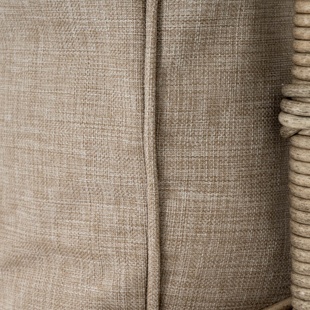 Close-up of the oatmeal cushion cover's woven texture and vertical piped seam beside pale frame wrapping.