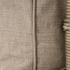 Close-up of the oatmeal cushion cover's woven texture and vertical piped seam beside pale frame wrapping.