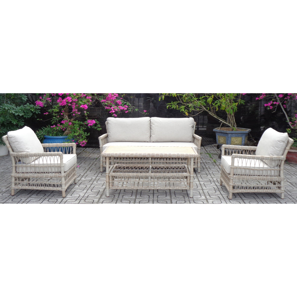 Pale wrapped lounge seating arranged with a sofa, two armchairs and a rectangular coffee table on patterned paving among flowering plants.