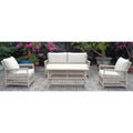 Pale wrapped lounge seating arranged with a sofa, two armchairs and a rectangular coffee table on patterned paving among flowering plants.